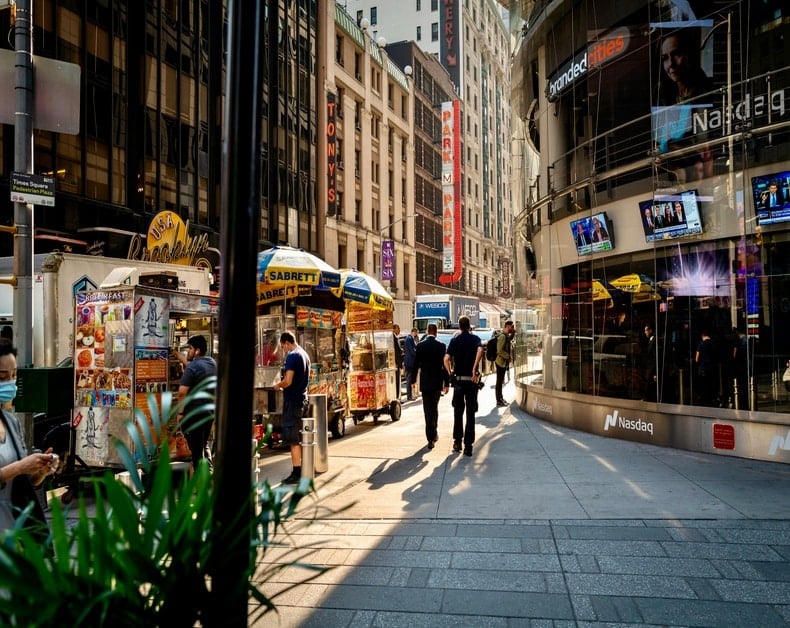 Busy urban street near Nasdaq with food stalls, pedestrians, and a glass-fronted building.