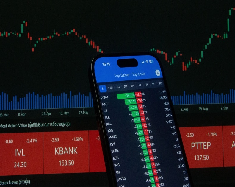 Smartphone displaying a stock trading app with green and red percent changes over a dark market chart backdrop