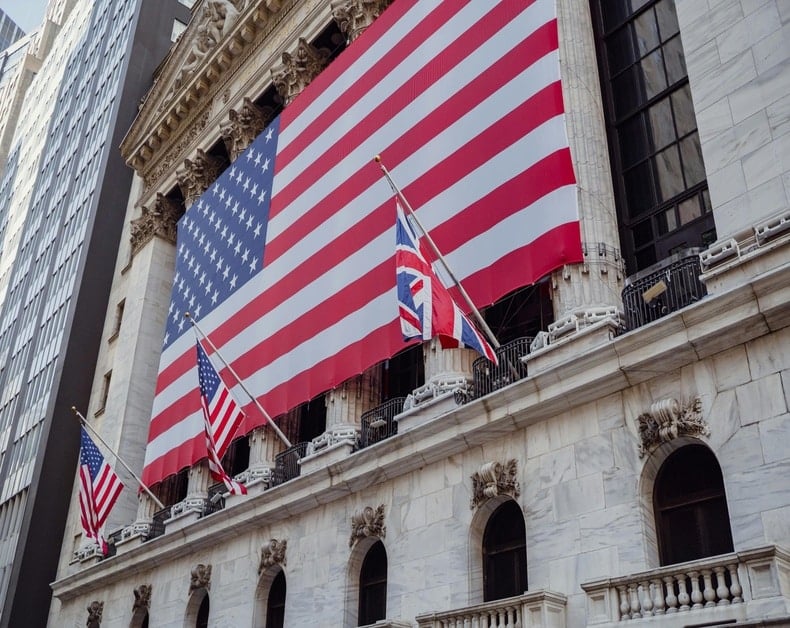 Large American flag draped across a historic stone building, with smaller flags in front.