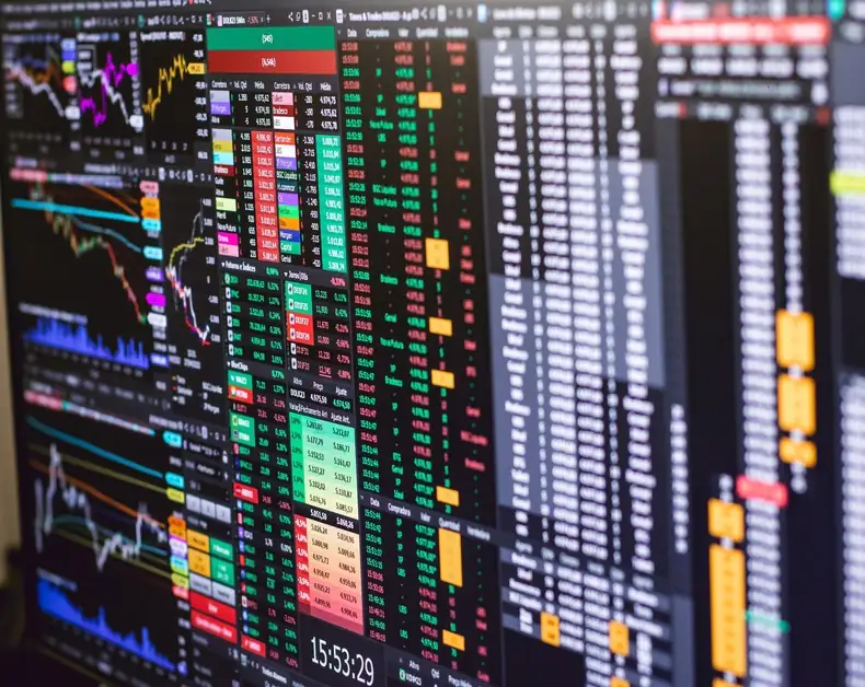 Stock market dashboard showing colorful charts, tables of numbers, and tickers on a dark screen.