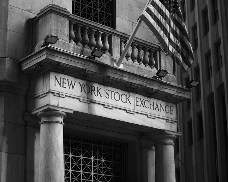 New York Stock Exchange entrance with columns and a waving American flag above the sign (black-and-white photo)